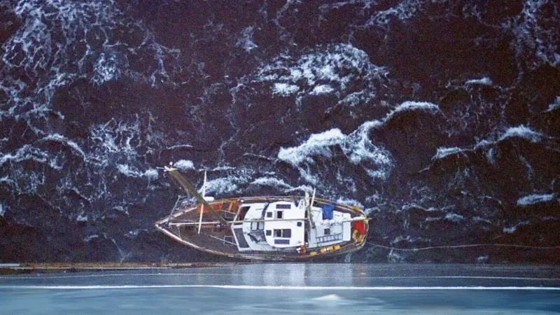 A small boat is dwarfed by the side of the ship attending its rescue