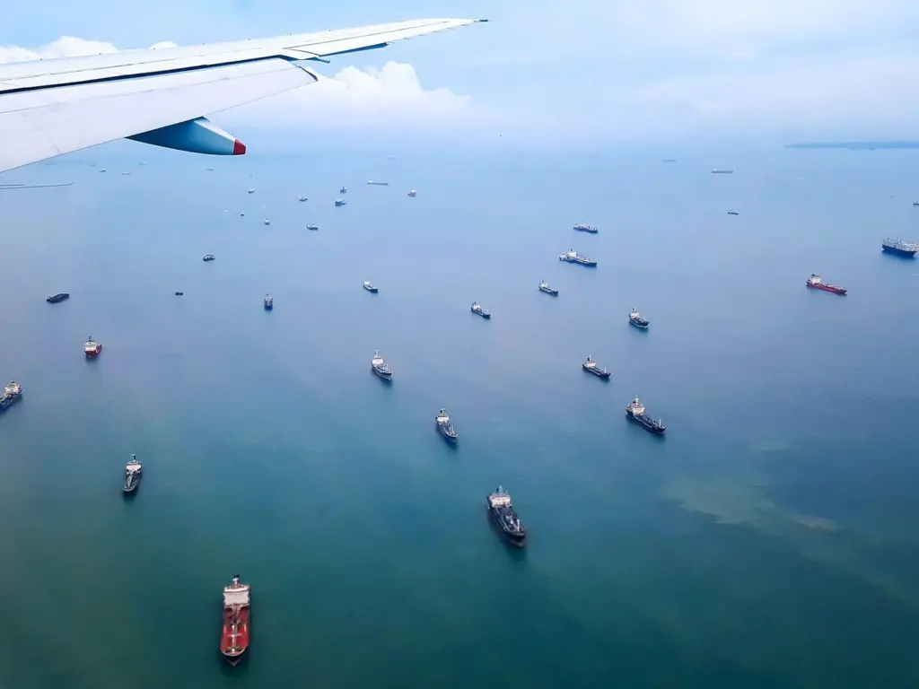 aircraft wing over ocean with a fleet of ships