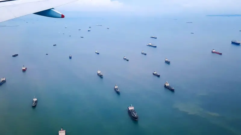 aircraft wing over ocean with a fleet of ships