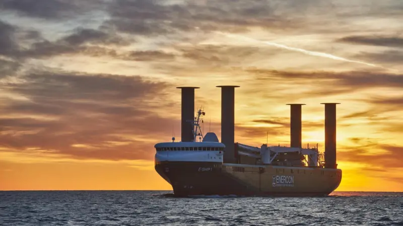 Wind-assisted cargo ship with four Flettner rotor sails at sea with a sunset behind