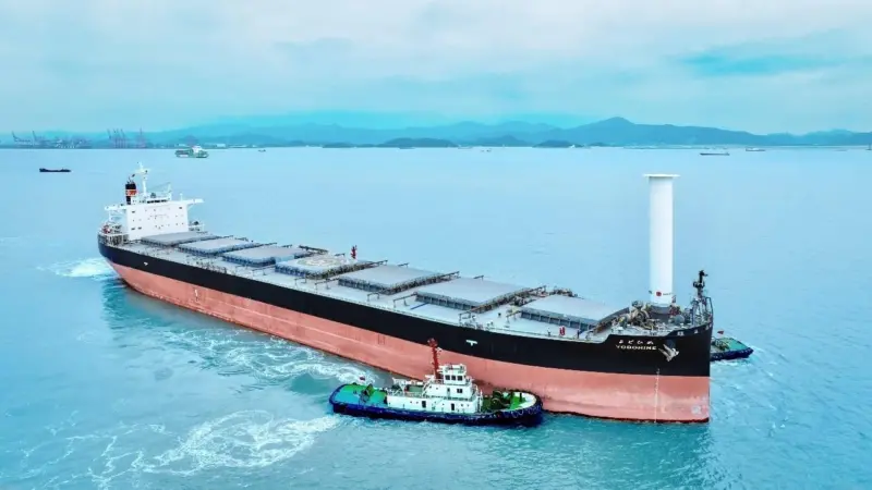 Bulk carrier Yodohime at sea featuring a single Rotor Sail at its bow and a tugboat alongside
