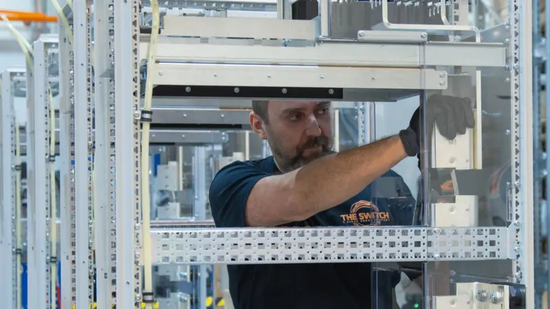 The image shows a technician in the process of assembling The Switch DC-Hub cabinets.