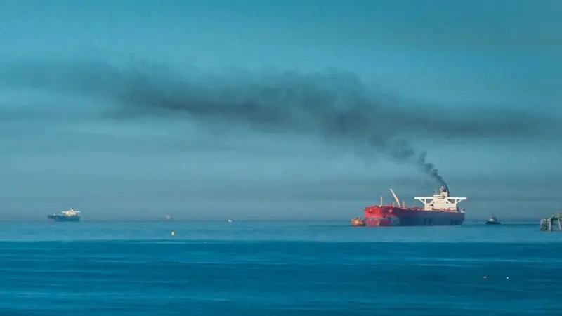 A ship at sea emitting black smoke