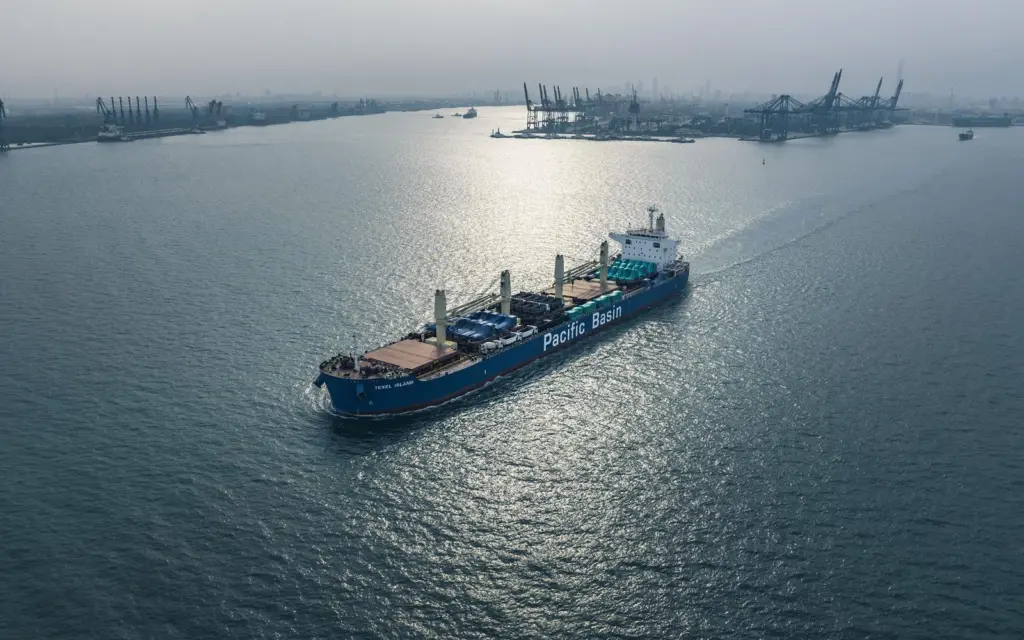 Pacific Basin ship at sea with port and cranes in background