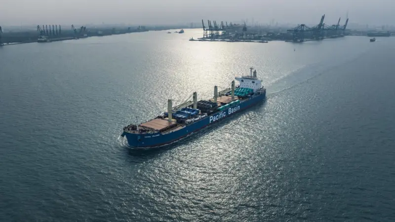 Pacific Basin ship at sea with port and cranes in background