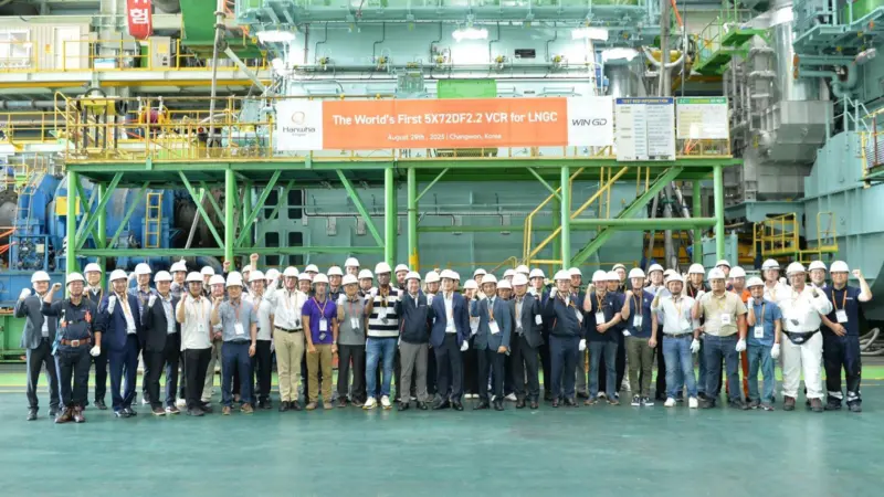 The image shows a group shot of WinGD and Hanwha Group employees in front of the LNG carrier engine