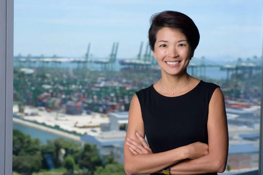 The photo shows Lynn Loo smiling for the camera in front of a port back drop