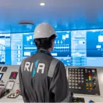 Man in hard hat and RINA boilet suit looking at ship bridge equipment